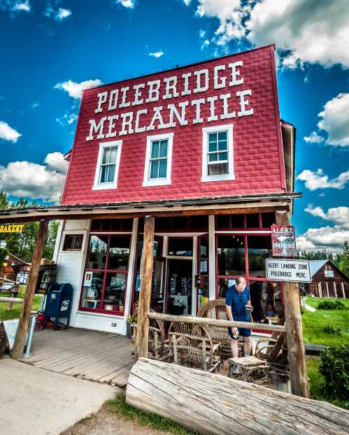 A red mercantile building with a sign, featuring a porch and a person outside, set against a blue sky with clouds.