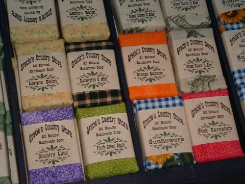 A display of handmade soaps in various colors and scents, each wrapped in decorative paper with labels.