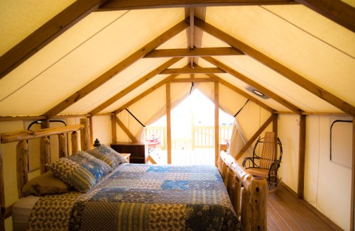 Cozy tent interior with a wooden bed, rocking chair, and natural light streaming in through the windows.