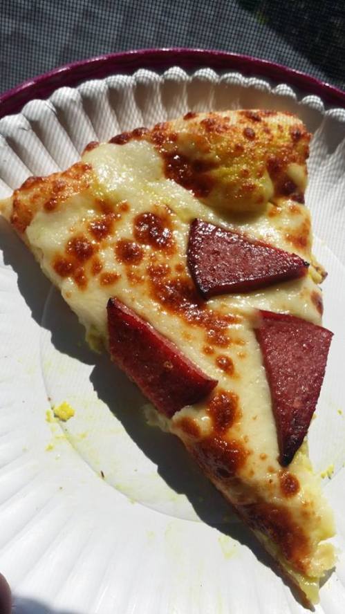 A slice of pizza topped with melted cheese and triangular pieces of pepperoni on a paper plate.