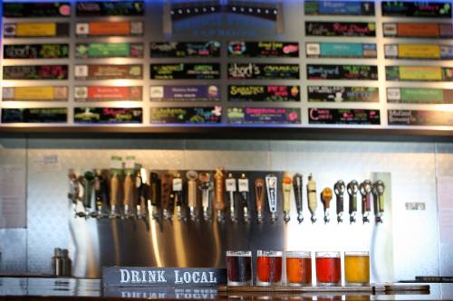 A bar with a variety of beer taps and a sign reading "Drink Local," featuring several glasses of different beers in front.