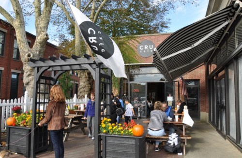 A cozy café with outdoor seating, surrounded by flowers and pumpkins, and people enjoying their time.