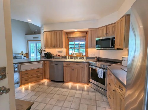 Bright kitchen with wooden cabinets, stainless steel appliances, and a window overlooking a scenic view.