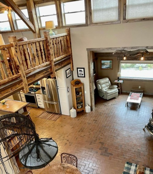 Cozy interior of a rustic home featuring a loft, wooden beams, and a warm color palette with brick flooring.