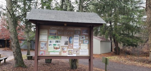 A nature center bulletin board displaying various informational posters surrounded by trees.