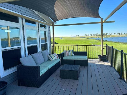 A cozy outdoor seating area with a sofa and coffee table, overlooking a green landscape and water under a blue sky.