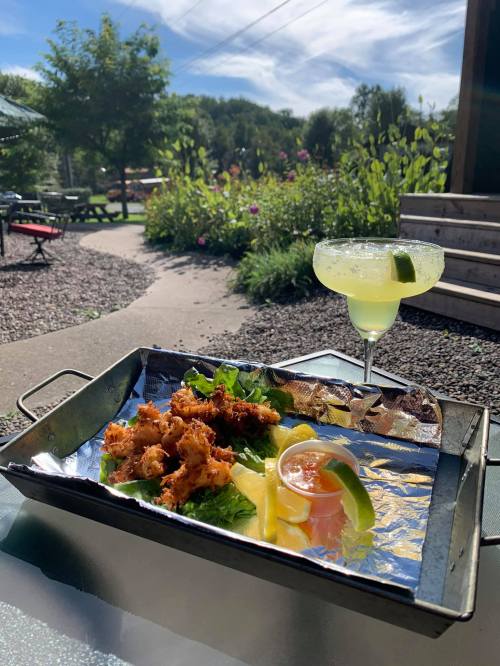 A tray with crispy fried food, garnished with lettuce and lemon, alongside a refreshing margarita in a garden setting.