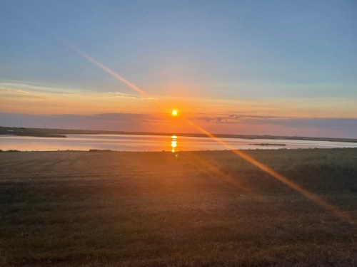 A serene sunset over a calm body of water, with vibrant colors reflecting on the surface and a grassy foreground.