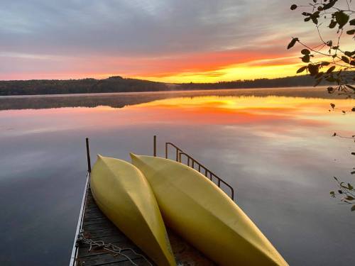 Two yellow kayaks rest on a dock by a calm lake, reflecting a vibrant sunset with colorful clouds.