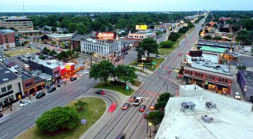 Aerial view of a bustling urban intersection with shops, trees, and traffic at dusk.