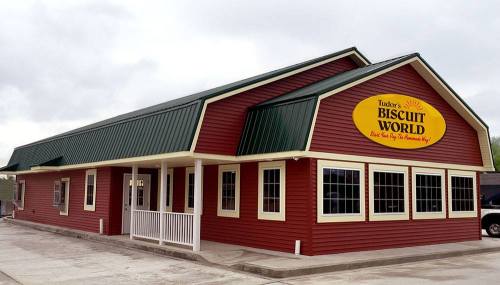 Exterior of Tudor's Biscuit World, a red building with a green roof and large sign, set against a cloudy sky.