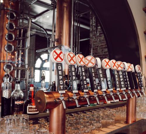 A row of beer taps with a mirrored backdrop and various bottles on the shelf behind them.