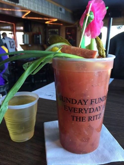 A large cocktail in a cup with a flower, pickles, and asparagus, next to a small shot glass on a table.