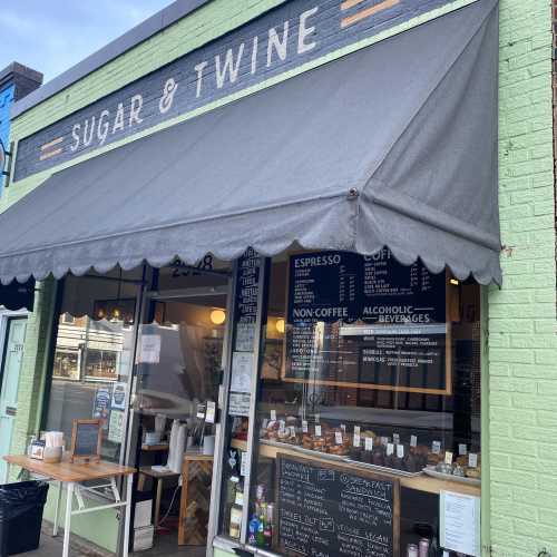 Exterior of a café named "Sugar & Twine," featuring a gray awning and a menu board with drink options.