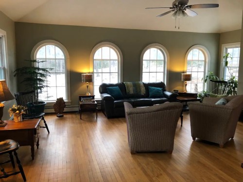Cozy living room with arched windows, a sofa, armchairs, and wooden furniture, featuring warm lighting and plants.
