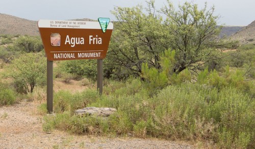 Sign for Agua Fria National Monument, surrounded by desert vegetation and rocky terrain.