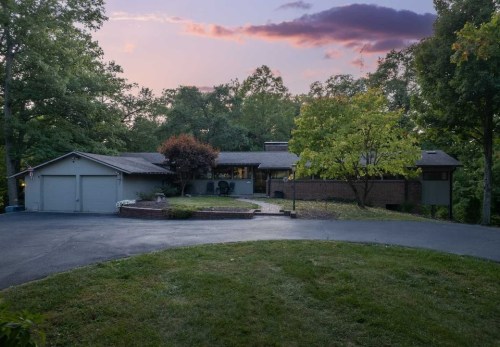 A modern home surrounded by trees, featuring a circular driveway and a sunset sky in the background.