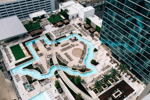 Aerial view of a modern hotel pool area with winding pools, lounge chairs, and palm trees.