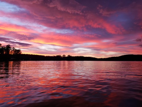 A vibrant sunset over a calm lake, with colorful clouds reflecting on the water's surface.