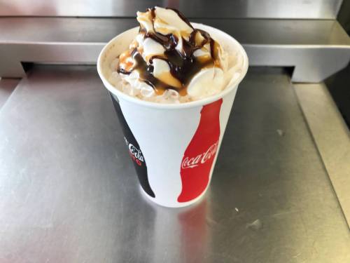 A cup of whipped cream topped with chocolate sauce and caramel, placed on a metallic surface.