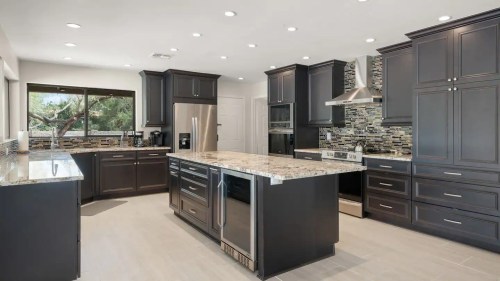Modern kitchen with dark cabinetry, granite countertops, stainless steel appliances, and a large island. Bright and spacious.