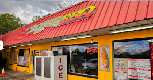 A colorful BBQ restaurant with a red roof, open sign, and large windows displaying menu items. Ice machine outside.