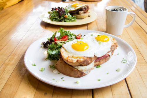 A plate with two sunny-side-up eggs on toast, served with a side salad and a cup of coffee in the background.