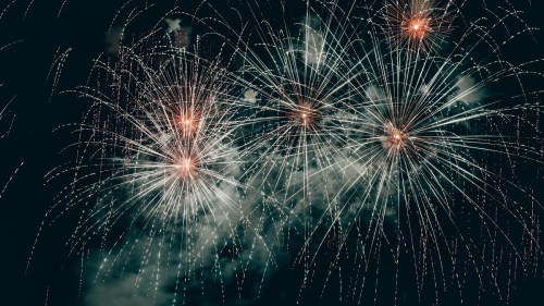 Colorful fireworks burst in the night sky, illuminating clouds with bright sparks and trails.
