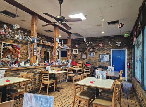 Cozy diner interior with wooden accents, patriotic decor, and empty tables under a ceiling fan.