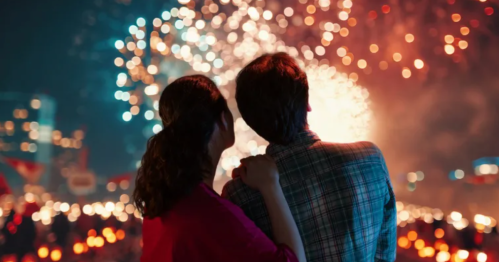A couple watches a colorful fireworks display together, surrounded by a festive atmosphere at night.