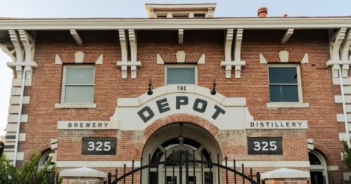 Historic brick building with "The Depot" sign, featuring brewery and distillery, and large arched entrance.