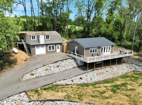 Aerial view of two houses on a landscaped property surrounded by trees and a gravel path.