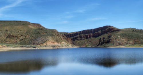 A serene lake surrounded by rocky hills under a clear blue sky, reflecting the landscape in calm waters.