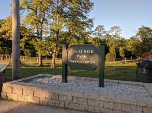 Sign for Halli Reid Park in Freeport Beach, surrounded by trees and grassy areas.