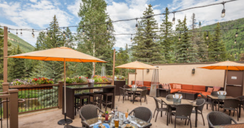 A scenic outdoor dining area with umbrellas, tables, and lush greenery in the background under a blue sky.