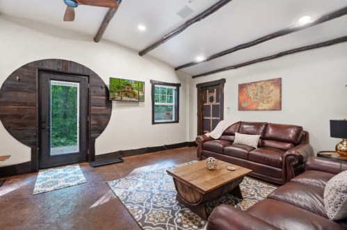 Cozy living room with leather sofas, wooden accents, and a round entryway, featuring a coffee table and decorative art.