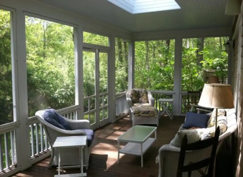 A cozy screened porch with comfortable seating, a coffee table, and greenery visible through the screens.