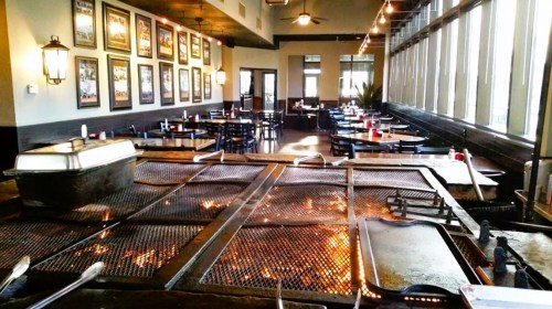 Interior of a restaurant featuring a grill, tables, and large windows with framed pictures on the walls.