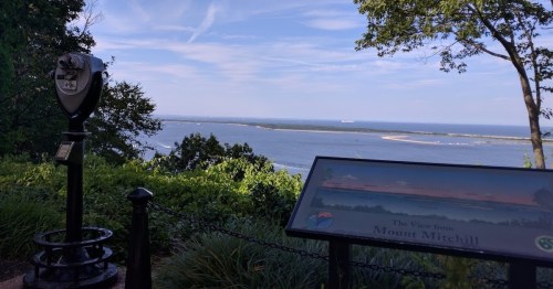 View from Mount Mitchell featuring a scenic landscape, a viewing telescope, and a sign about the area.