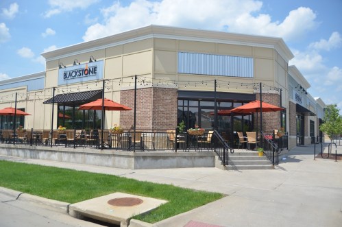 Exterior view of a restaurant named Blackstone, featuring outdoor seating with orange umbrellas and a landscaped area.