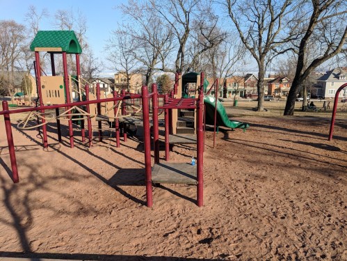 A playground with climbing structures and slides, surrounded by bare trees and a clear blue sky.