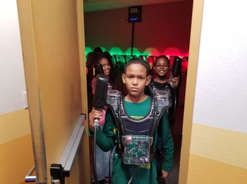 A group of kids in laser tag gear, with one boy in the foreground holding a laser gun, ready to play.