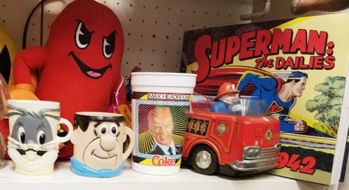 A collection of vintage toys and mugs, including a Superman book, cartoon character mugs, and a toy fire truck.
