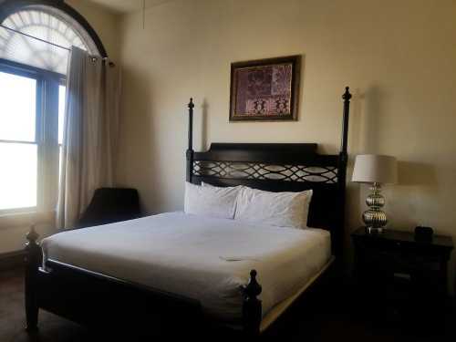 A cozy bedroom featuring a four-poster bed, a lamp, and a framed artwork on the wall near a large window.