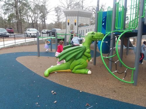 Children playing on a colorful playground with a green dragon sculpture and climbing structures.