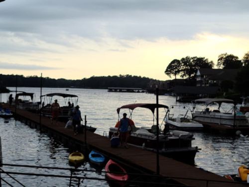 A serene lakeside scene at dusk with boats docked and people enjoying the waterfront.