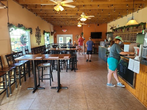 A spacious restaurant interior with wooden tables, chairs, and a counter; patrons are seated and ordering.