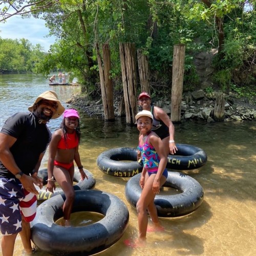 A group of four people, including children, enjoying a sunny day by the water, sitting in inner tubes.