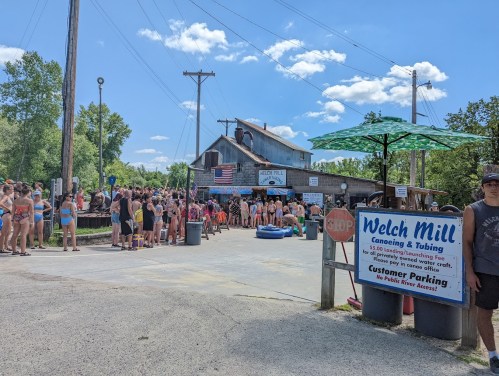 A busy outdoor scene at Welch Mill with people in swimsuits waiting in line for canoeing and tubing activities.