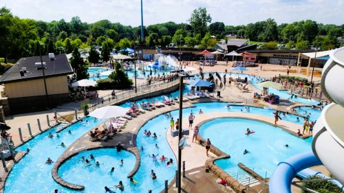 Aerial view of a busy water park with pools, slides, and people enjoying the sunny day.